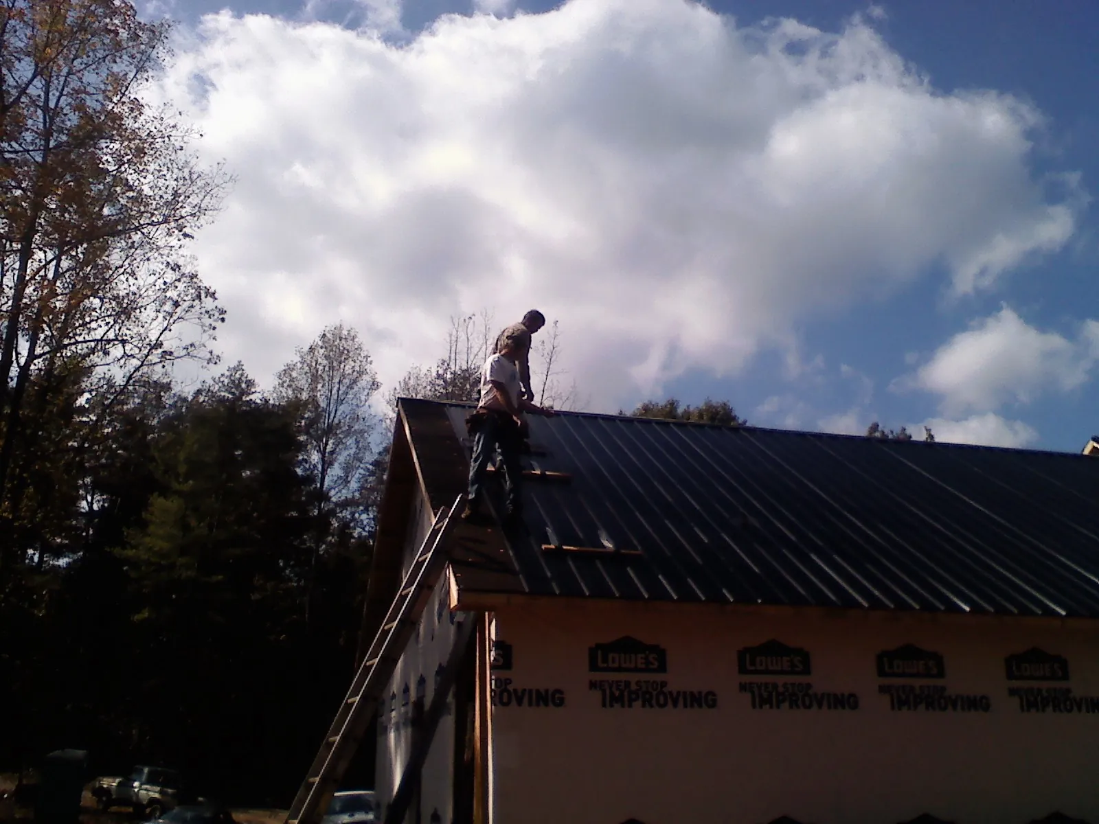 Roofer fastening dark metal panels high against a cloudy sky, from a Roof Inspection job in Grafton